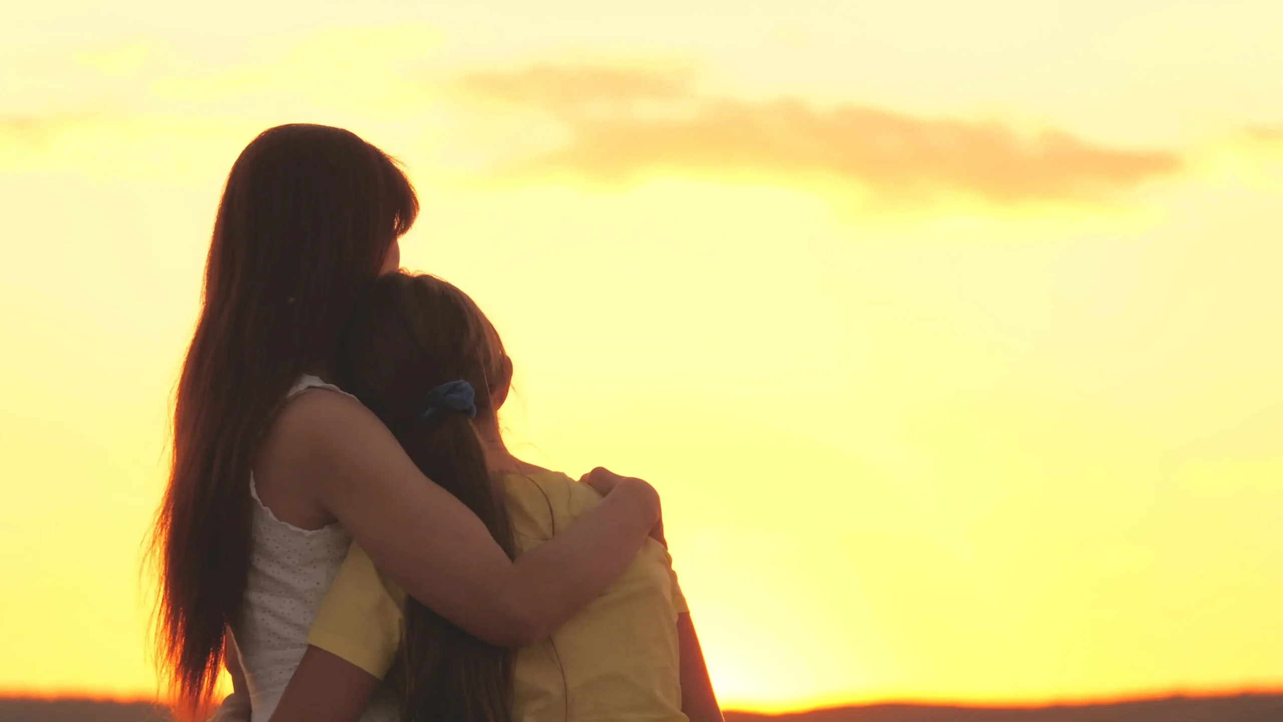 Young women and daughter looking into sunset grieving together.