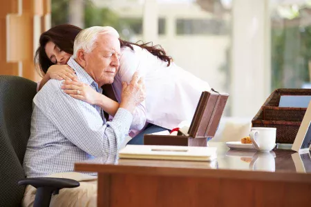 Elderly man receiving bereavement gift from daughter and comforting hug.
